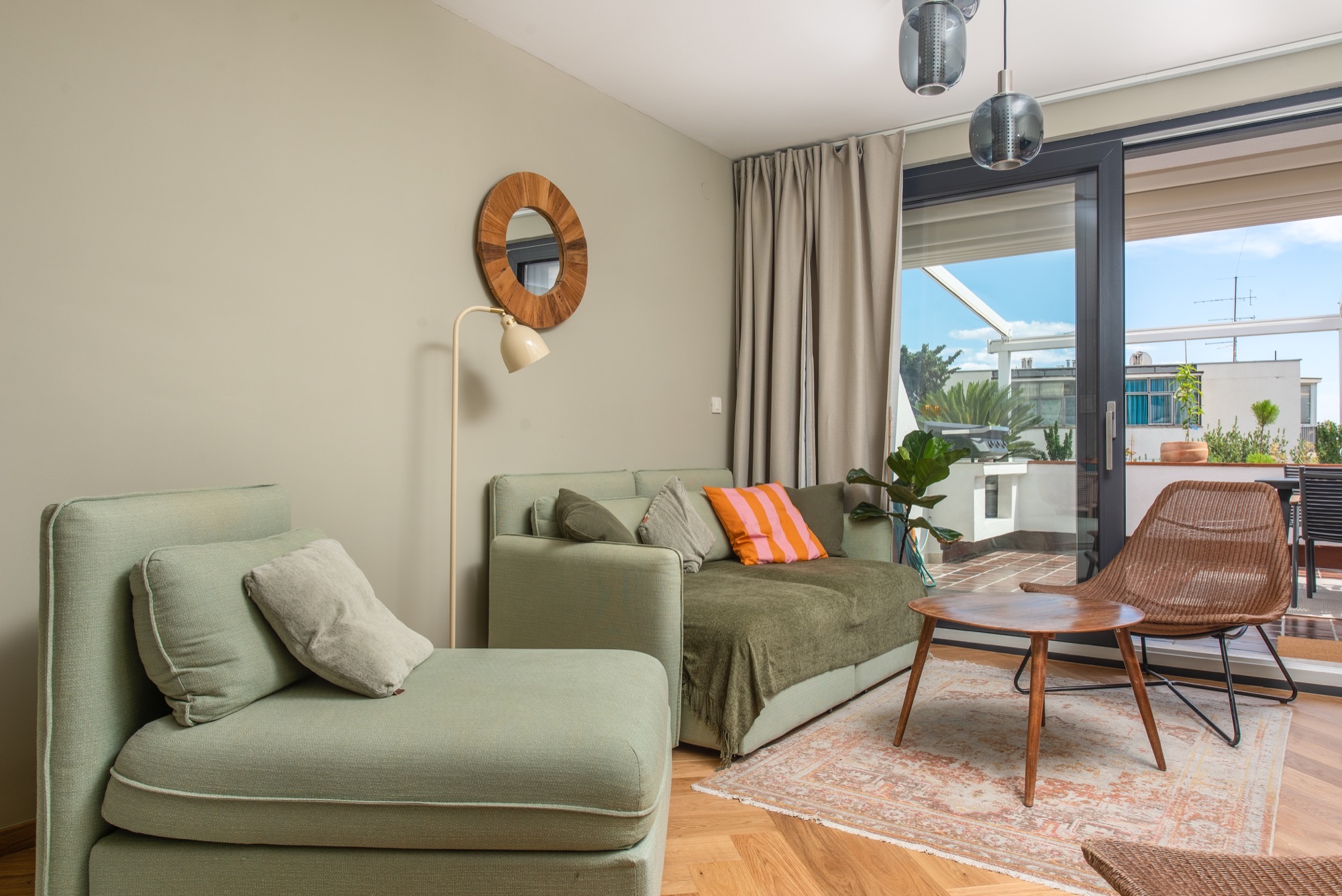 Bright living room with sage sofa, rattan chair, and terrace beyond