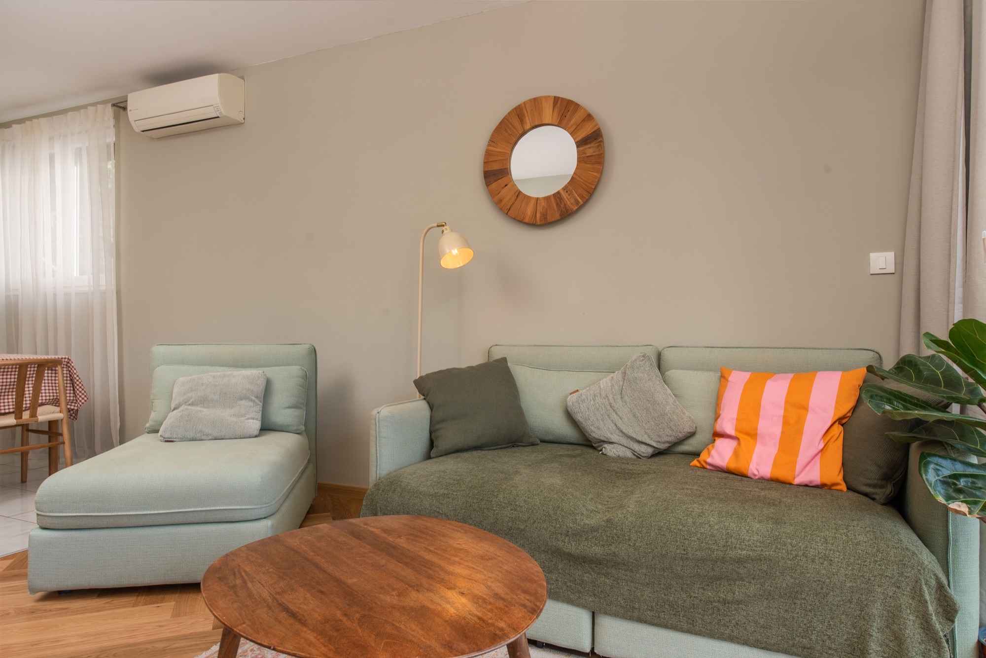 Sage green sofa with striped cushion and a round wooden sunburst mirror
