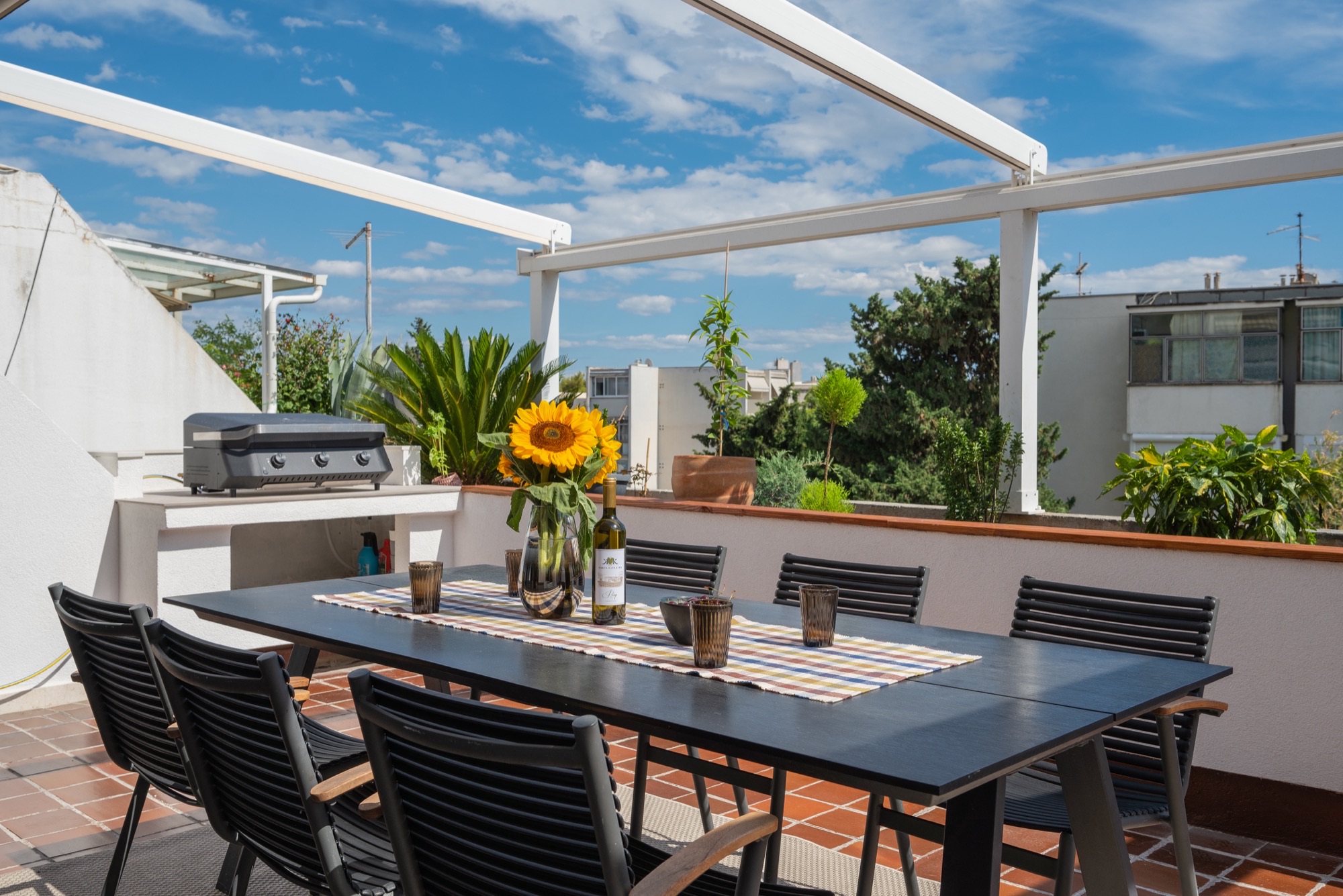 Rooftop terrace dining with sunflowers, wine glasses, and a clear blue sky