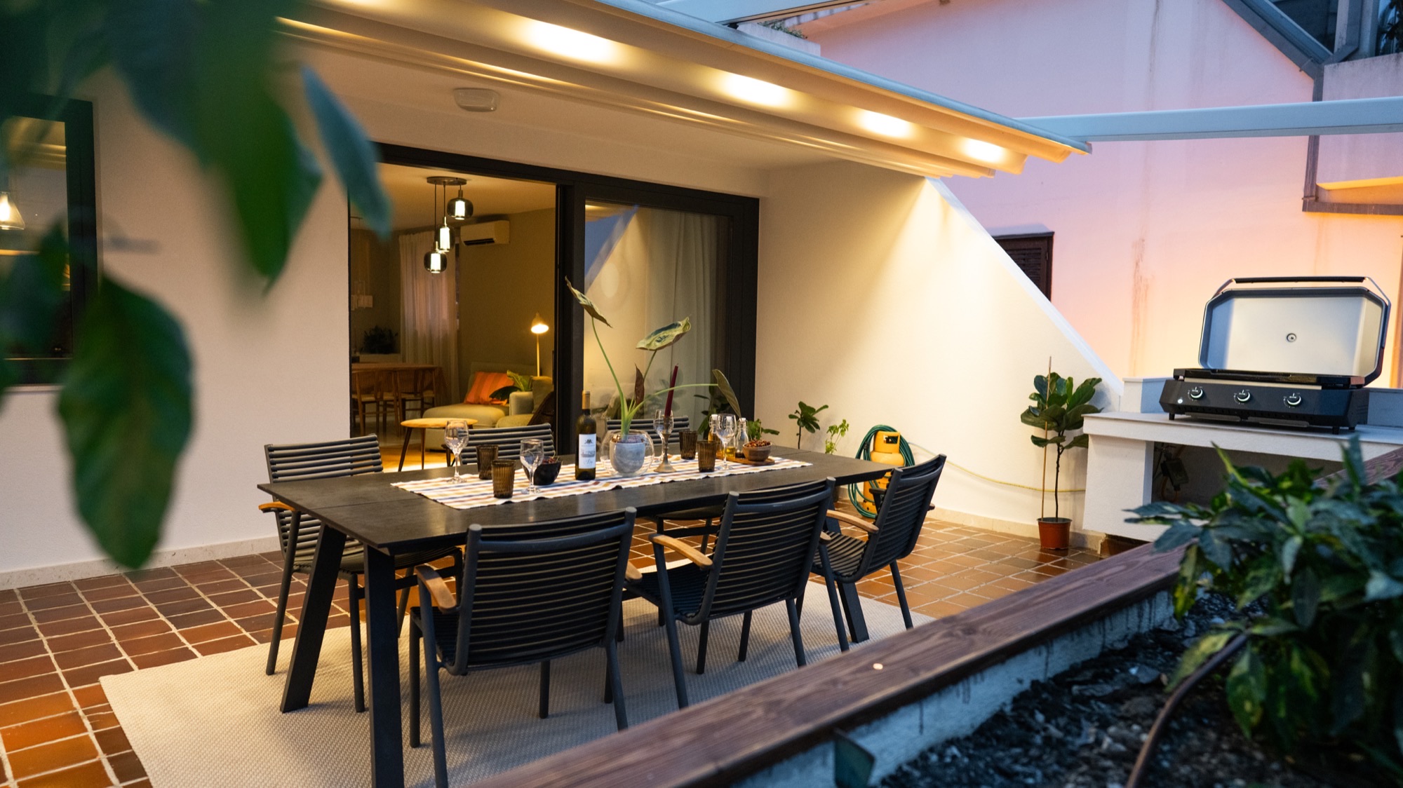 Spacious terrace at dusk with a dining set for six, gas grill, and warm LED awning lights